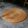 Round woven mat on a gray floor with greenery in the background