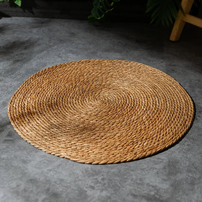 Round woven mat on a gray floor with greenery in the background